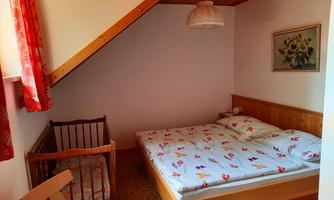 A cozy bedroom with a double bed and a baby crib. The walls are painted in warm colors and there is a window with curtains.