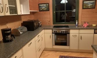 A modern kitchen with wood paneling and a large window front. Various kitchen appliances are on the countertop and a rug lies on the floor.