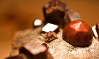 A close-up of shiny minerals on a piece of rock. The most striking crystals are red and have a faceted shape.