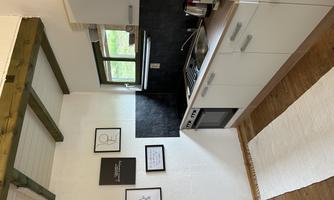 A modern kitchen with white cabinets and wooden shelves. There is a window that lets in natural light, and decorative pictures on the wall.