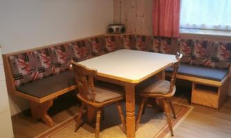 A cozy dining area with a wooden table and a bench. The walls are paneled with wood, and the room is decorated with a carpet.