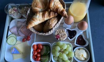 A breakfast tray with fresh croissants, eggs, yogurt, fruit, and cheese. On the side, there is a glass of freshly squeezed orange juice.