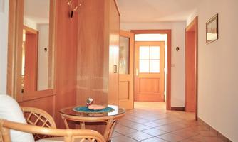A bright hallway with wooden details and a cozy corner. The entrance door is clearly visible and inviting.