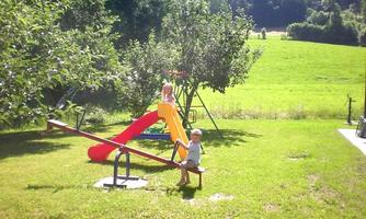 A beautiful playground with a slide and a seesaw. In the background, green meadows and trees can be seen.
