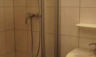 A small bathroom with a shower and a sink. The walls are tiled and there is a mirror above the sink.