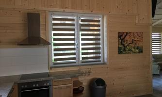 A modern kitchen with wooden paneling and large windows. A colorful painting hangs on the wall.