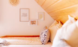 A cozy room with a sloped ceiling and soft pillows. Decorative pictures and a sun symbol are hanging on the wall.
