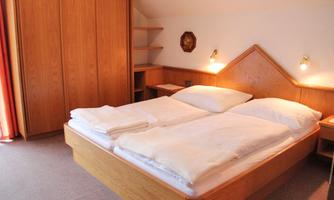 A cozy bedroom with a large wooden bed and two beds. The walls are light and there is a wooden dresser in the background.