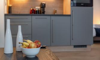 A modern kitchen with gray cabinets and a wooden table. On the table sits a bowl of apples and bananas as well as two stylish vases.