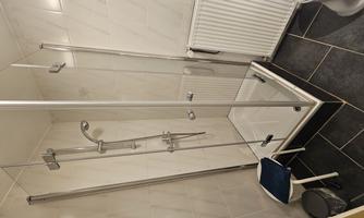 A small modern shower cabin with clear glass walls. The room also contains a toilet and a radiator.