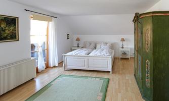 A bright bedroom with two white beds and a rustic dresser. The room has large windows that let in natural light.