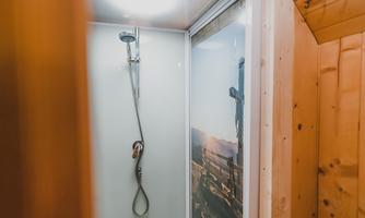A modern shower with a glass partition and a showerhead. The interior is surrounded by wooden panels.