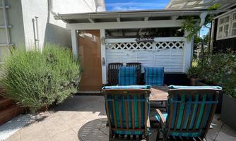 A cozy outdoor area with chairs and a table. Surrounded by plants and a clear blue sky.