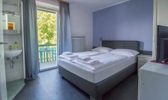A modern bedroom with a double bed and white bedding. The room has large windows overlooking a balcony and offers an inviting atmosphere.