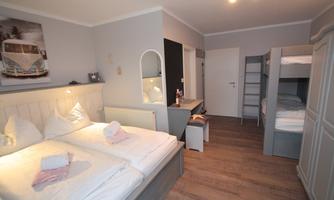 An inviting bedroom with two single beds and a bunk bed. Bright walls and wooden flooring create a cozy atmosphere.
