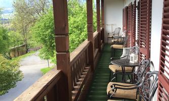 A beautiful balcony with wooden features and chairs. In the background, green trees and a quiet street can be seen.