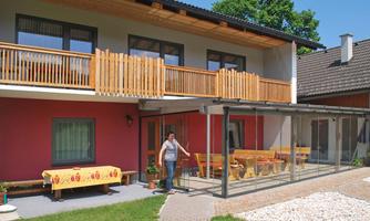 A modern house with a beautiful balcony and a glazed seating area. In the foreground, there is a person at a table with flowers.