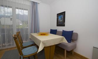 A bright dining area with a table and chairs. A picture hangs on the wall, and large windows let in a lot of light.