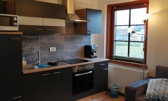A modern kitchen with dark cabinets and a stove. There is a window with plenty of natural light and a cozy living area with a sofa.