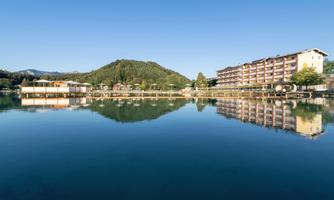 A serene lake surrounded by green hills and modern buildings. The reflection on the water's surface enhances the peaceful atmosphere.