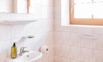 A modern bathroom with white tiles and a wooden ceiling. It features a sink, a toilet, and a window.