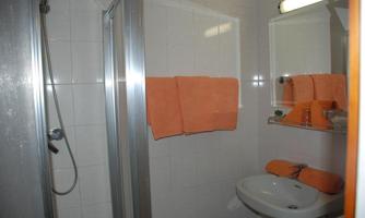 A small bathroom with a shower and a sink. Orange towels are neatly placed on a shelf.
