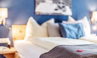 A cozy bedroom with a large bed and soft pillows. The walls are painted a deep blue, and gentle lamps are attached.