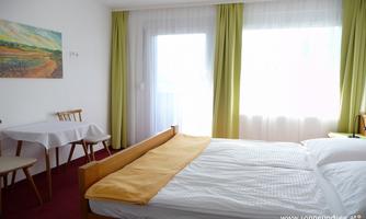 A bright and cozy room with a double bed and a small dining area. Large windows let in plenty of daylight, and the room is tastefully decorated.