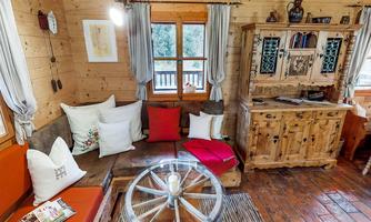A cozy living space with wood paneling and a comfortable seating area. A round table with a rustic style and decorative cushions complement the warm atmosphere.