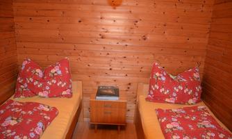 A cozy room with two single beds and red flower cushions. There is wood paneling on the wall.