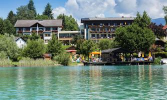 A picturesque lake landscape with a hotel in the background. Surrounded by trees and loungers by the water, the place invites you to relax.