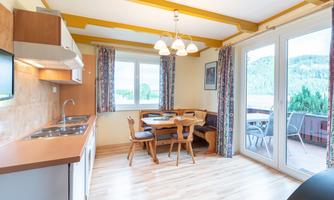 A bright kitchen with a dining table and chairs. Large windows provide a view of nature.