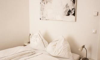 An inviting bedroom with a comfortable bed and artistic wall design. The soft colors and minimalist decor create a relaxed atmosphere.
