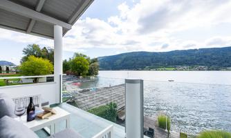 A beautiful view of a tranquil lake with green shores. In the foreground, there is a terrace and cozy seating.
