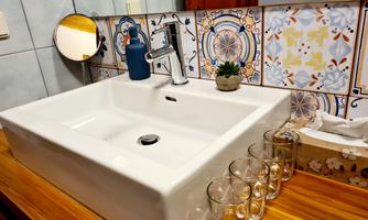A modern bathroom with a white sink and a stylish faucet. In the background, decorative tiles and a small plant can be seen.
