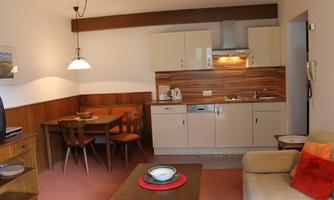 A cozy kitchenette with a dining area and a living room. The decor is modern and friendly.