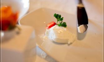 A dessert on a plate with a serving of cream, garnished with a small piece of tomato and fresh parsley. The plate is elegantly arranged and looks appetizing.