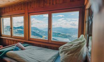 A cozy bedroom with a bed and a beautiful view from the window of the mountains and the lake. The wooden paneling creates a warm, inviting atmosphere.