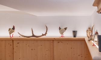 A decorative wooden shelf with several chicken figures and a antler. The lighting creates a cozy atmosphere.