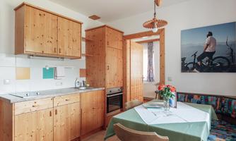 A cozy kitchen with wooden furniture and a dining table. A picture of a cyclist hangs on the wall.