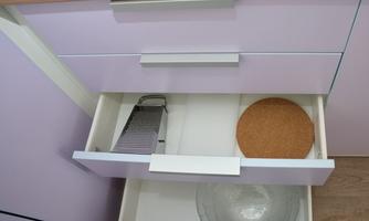 A kitchen drawer with a grater, a round coaster, and a transparent bowl. The drawer has a bright purple color.