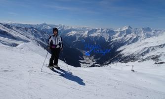 A person stands on a snowy slope and is ready to ski. In the background, impressive mountain landscapes can be seen.