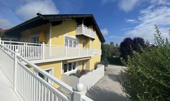 A beautiful yellow house with a balcony and a terrace.  
Surrounded by green vegetation and a clear blue sky.