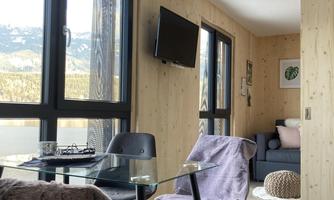 A modern living space with large windows and a beautiful view of the mountains. There are chairs at the table, and a cozy seating area invites you to relax.