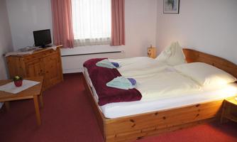 A cozy bedroom with a large bed and wooden furniture. The room has a television and is bright with a window that lets in daylight.