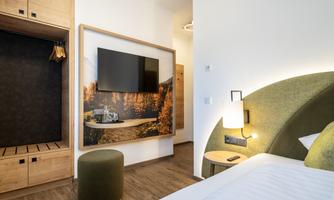 A modern hotel room with a cozy bed and a large television. On the wall hangs a picture of an autumn landscape.
