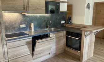 A modern kitchen with wooden cabinets and an elegant, metallic work area. The equipment includes a stove, a dishwasher, and a sink.