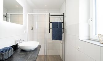 A modern bathroom with a shower and a sink. The walls are brightly tiled, and a towel hangs on a black holder.