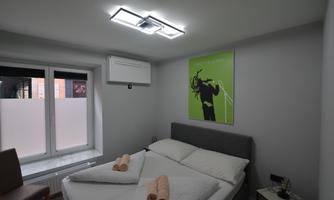 A modern bedroom with a double bed and a painting on the wall.  
Windows provide a lot of natural light and there are fresh towels on the bed.