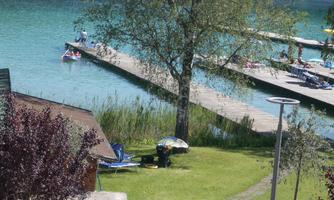 A calm lake with crystal clear water and wooden walkways. In the foreground, there are lounge chairs and a tree.